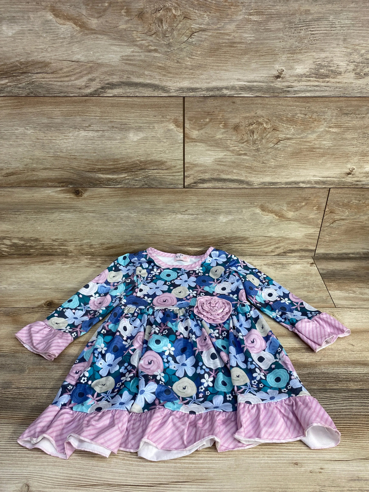 Long-sleeve baby dress with blue, purple floral pattern and pink striped ruffles on wooden floor