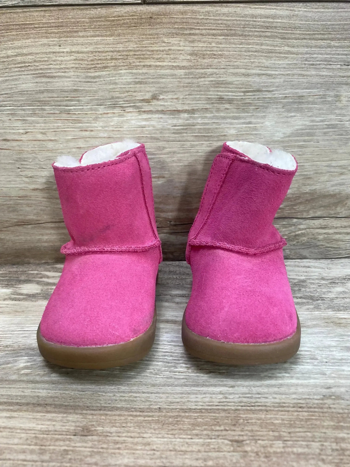 Front view of UGG Keelan boots size 2c 3c in pink suede with shearling lining and side bow on wood plank floor