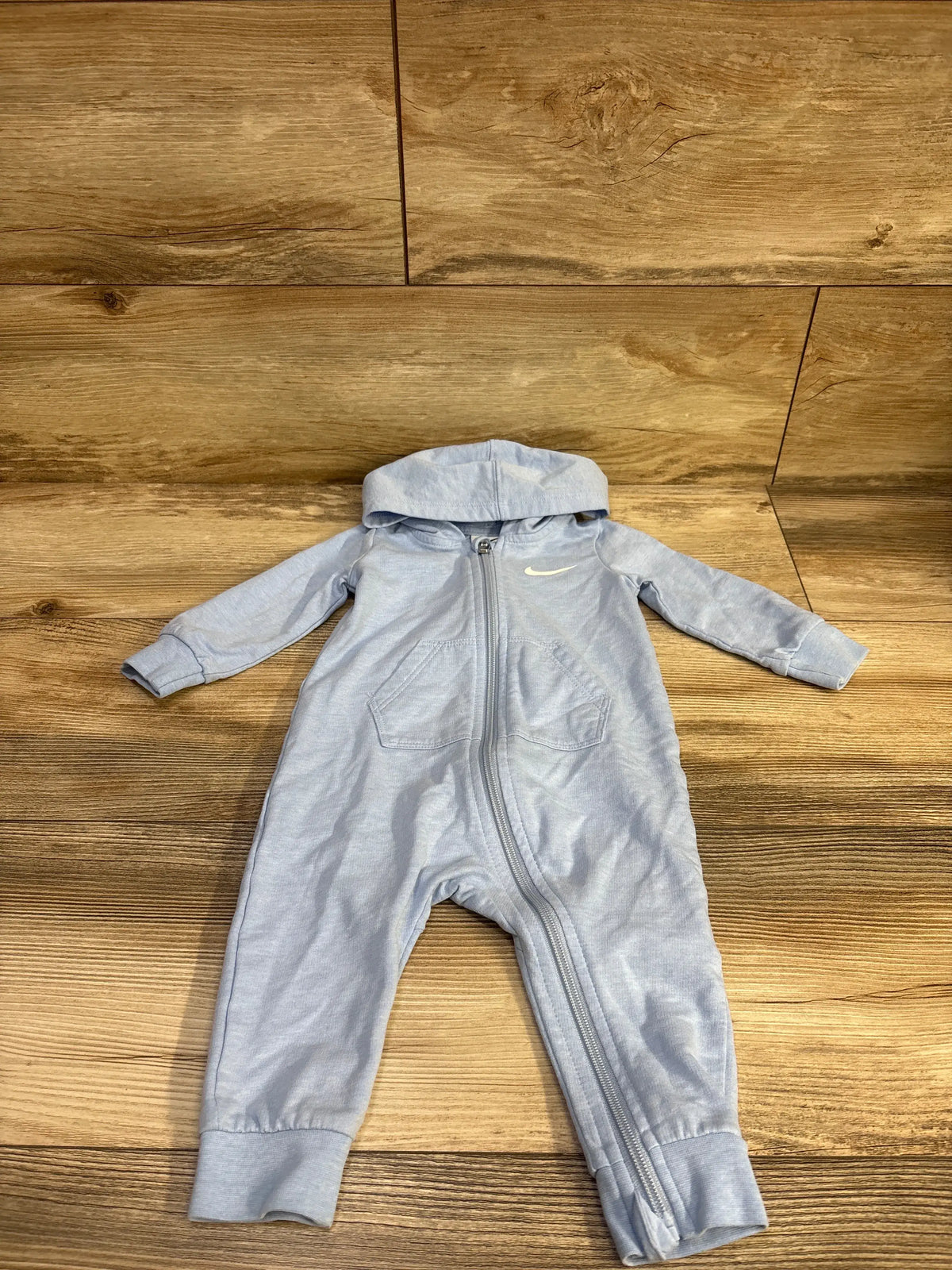 Front flat lay of Nike hooded coverall with diagonal zipper, front pockets, cuffed sleeves and ankles on wood background