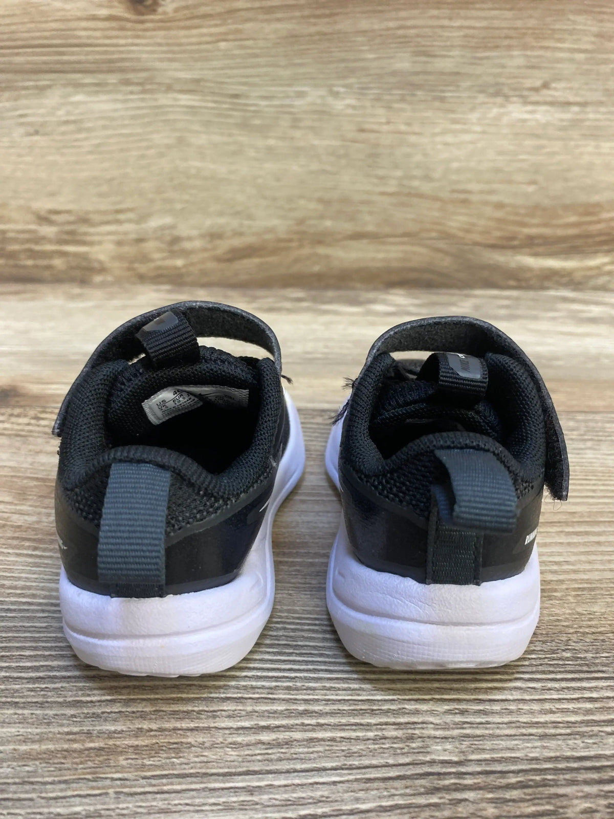 Back view of Nike Cosmic Runner TD toddler sneakers size 4C showing black upper, heel pull tabs and white soles on wood floor