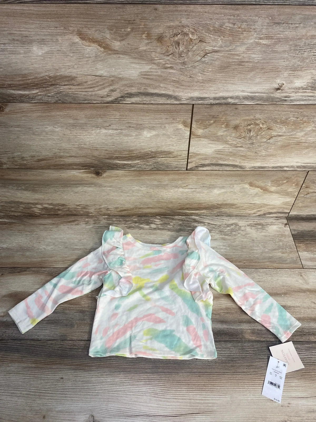 Toddler long-sleeve tie-dye shirt with ruffle detailing on wooden floor