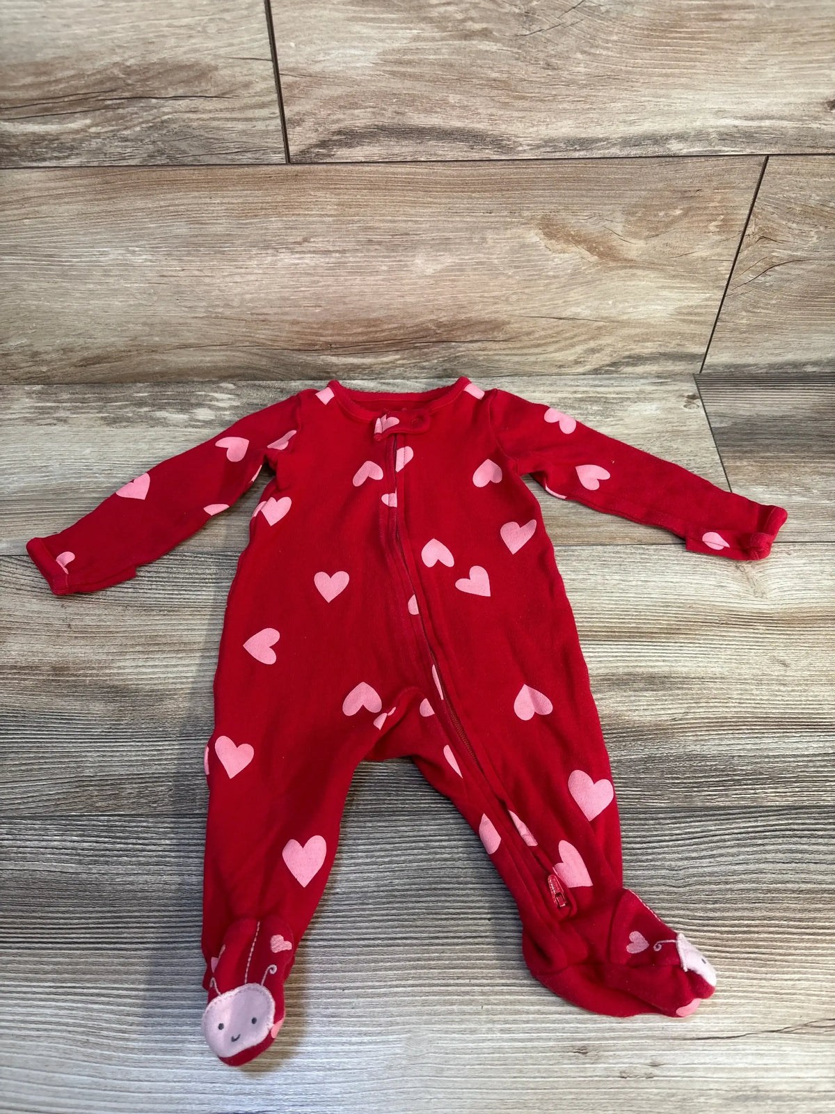 Red baby sleeper with pink heart print and character feet on wood floor
