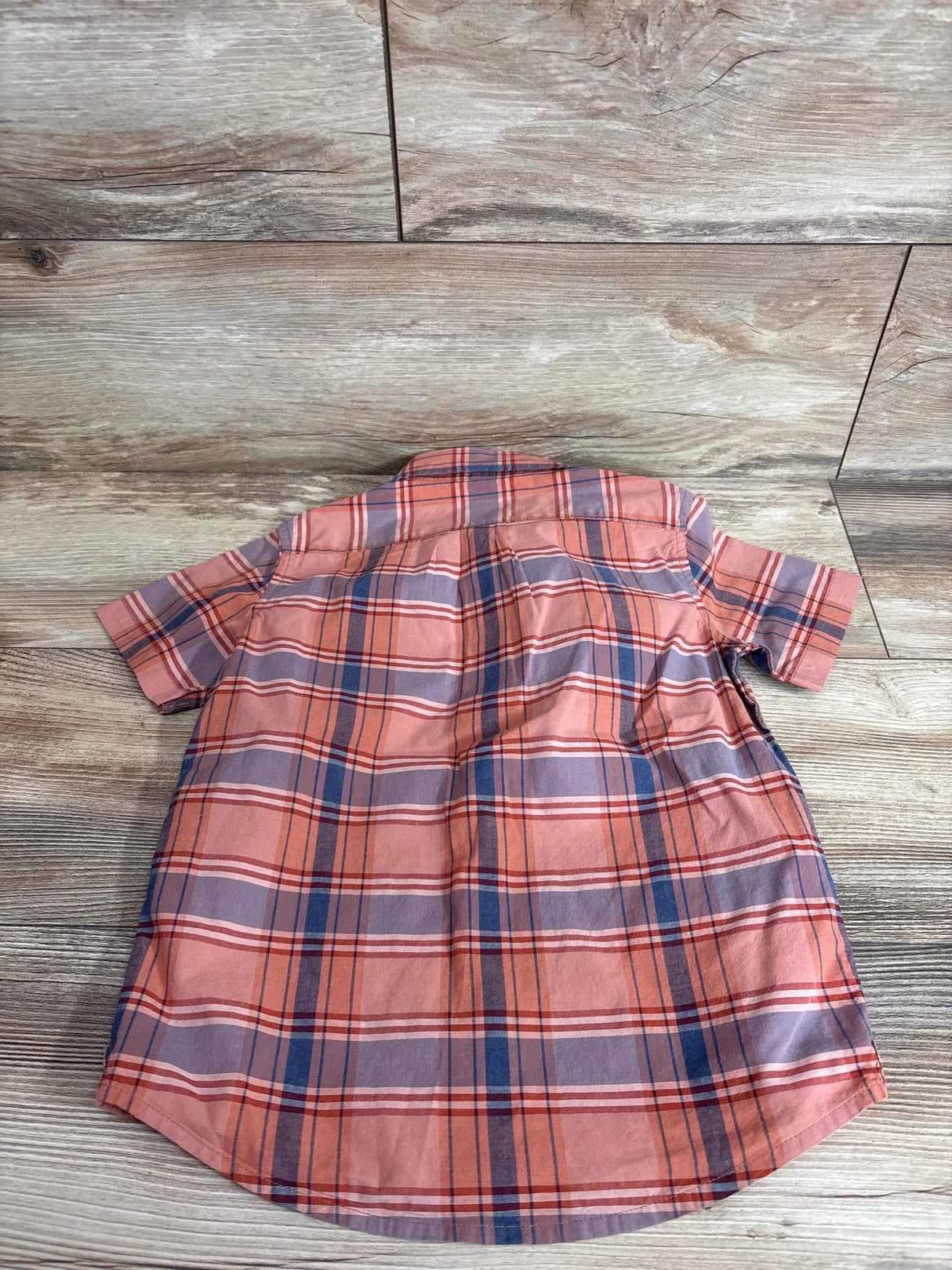 Back view of toddler orange and blue plaid poplin short-sleeve button-down shirt laid flat on wood background