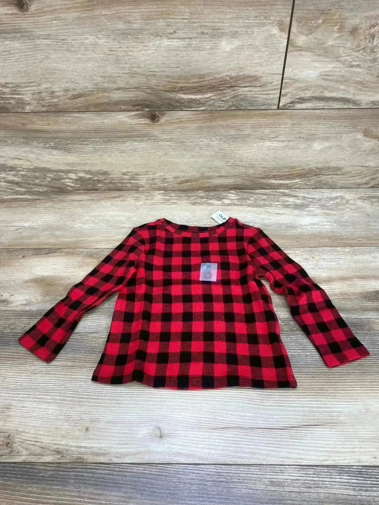 Flat-lay of Old Navy toddler long-sleeve buffalo check shirt in red and black, size 2T, showing crew neck and straight hem on light wood background