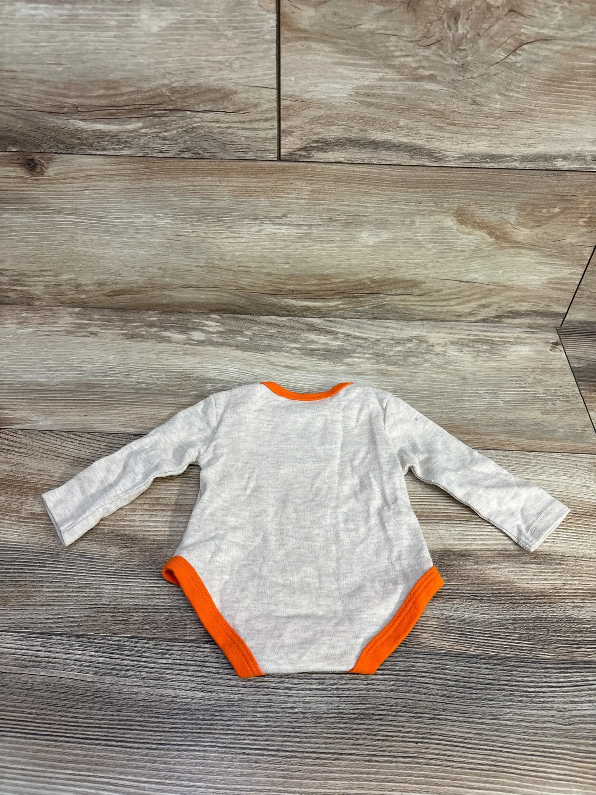 Gray long sleeve baby bodysuit with orange trim on wood floor