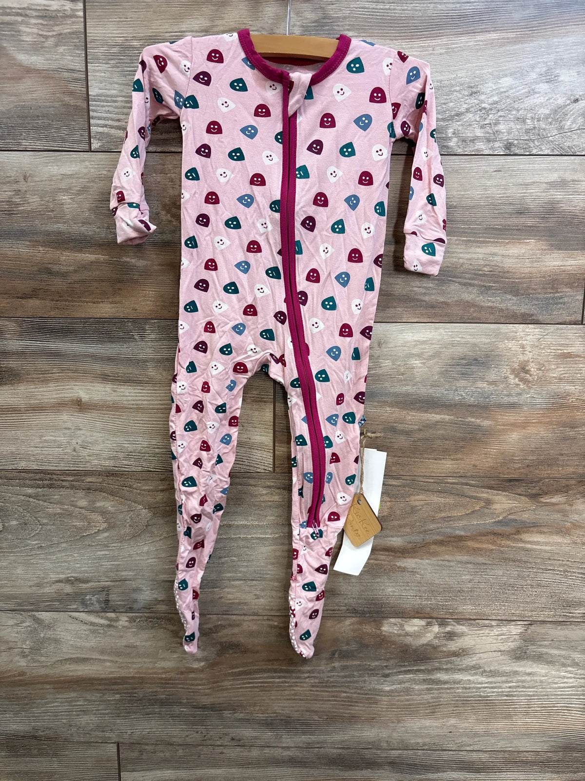Front view of pink Happy Gumdrops zip footie with long sleeves, full length zipper, and gumdrop pattern on wood floor