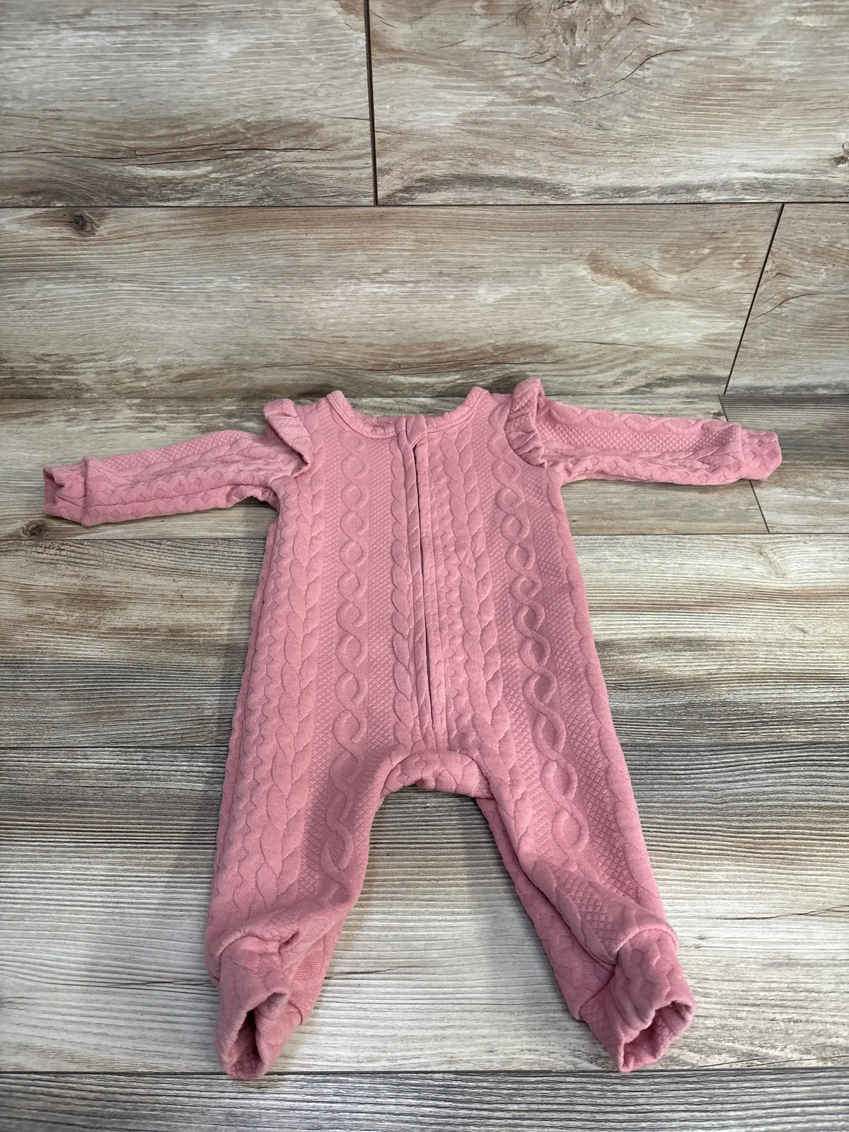 Pink cable knit long sleeve baby romper with ruffle shoulders on wood background