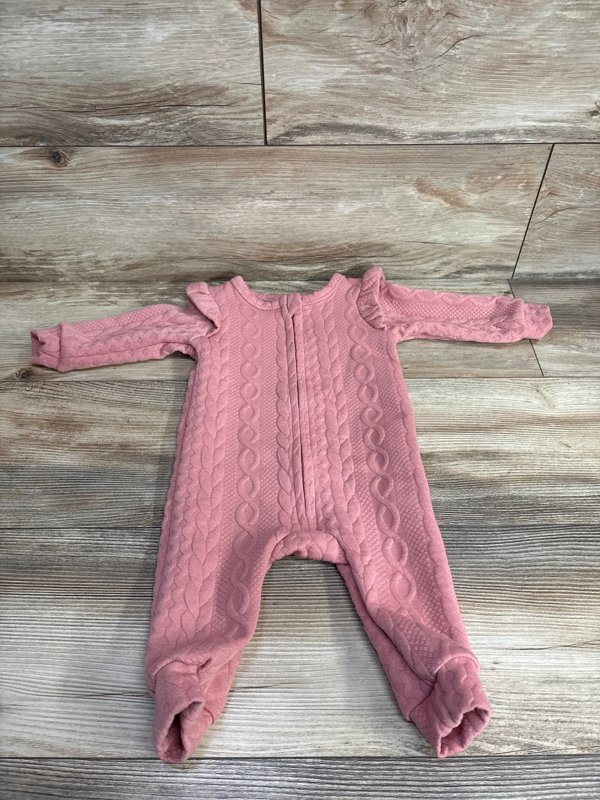 Pink cable knit long sleeve baby romper with ruffle shoulders on wood background