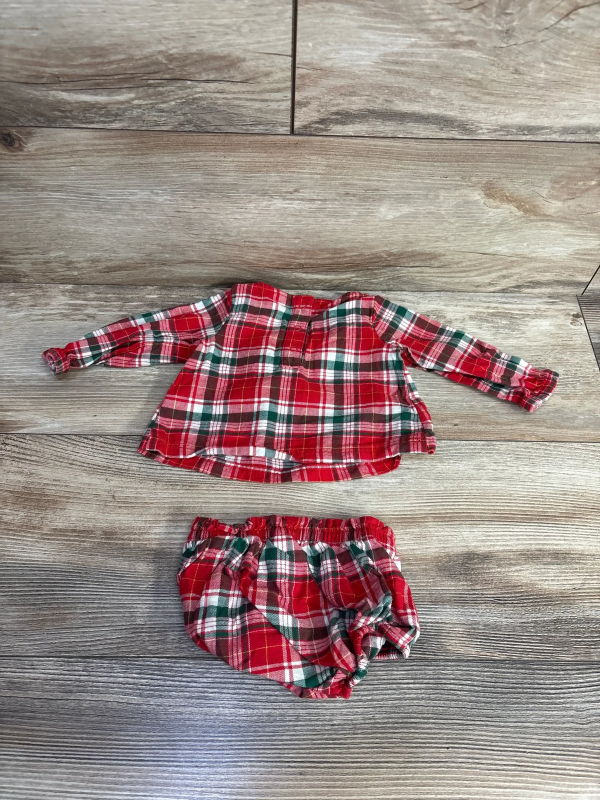 Flat lay of newborn red plaid ruffled long-sleeve top showcasing ruffle trim with matching elastic-waist bloomers on wood floor