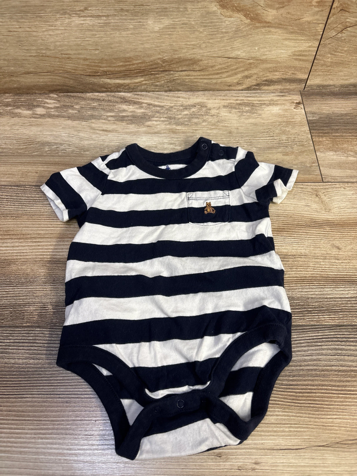 Flat lay of Baby Gap navy and white striped pocket bodysuit (6-12 months) showing front pocket and snap crotch on wood floor