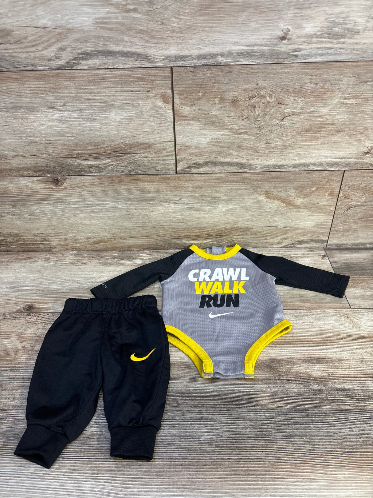Nike baby outfit set with 'Crawl Walk Run' bodysuit and black pants on wood floor