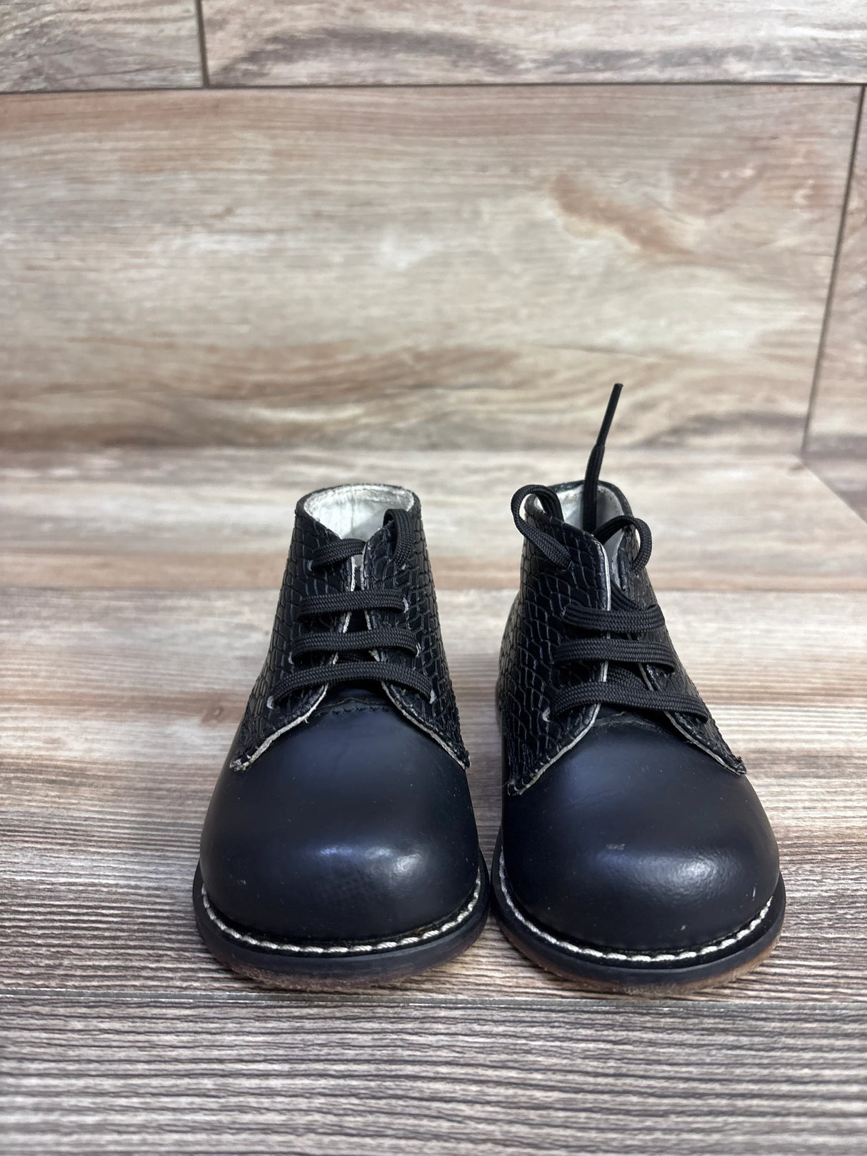 Black toddler lace-up boots with textured sides on wood floor