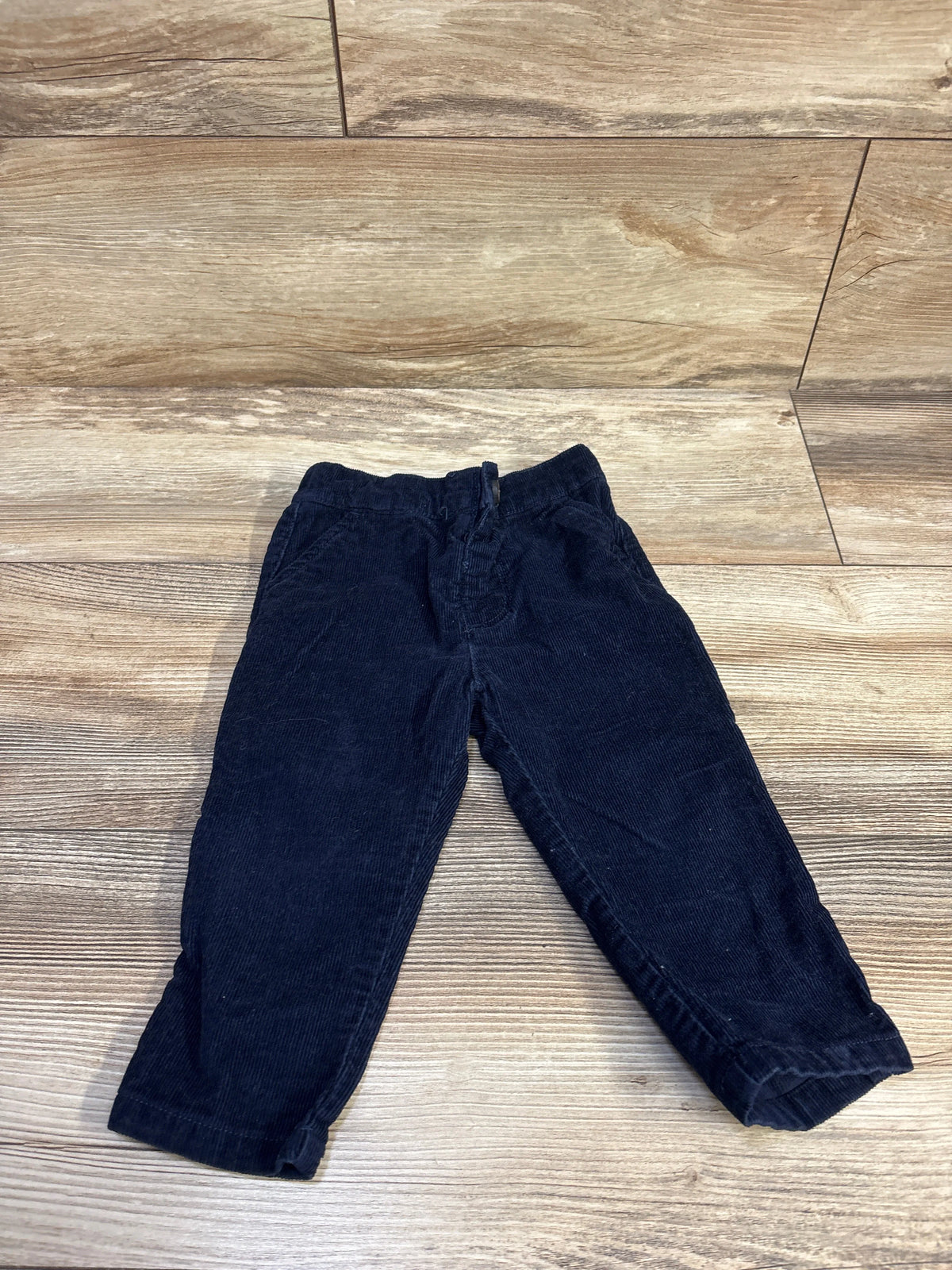Flat lay of navy corduroy toddler pants, size 12-18 months, elastic waistband and cuffed hems on wood background