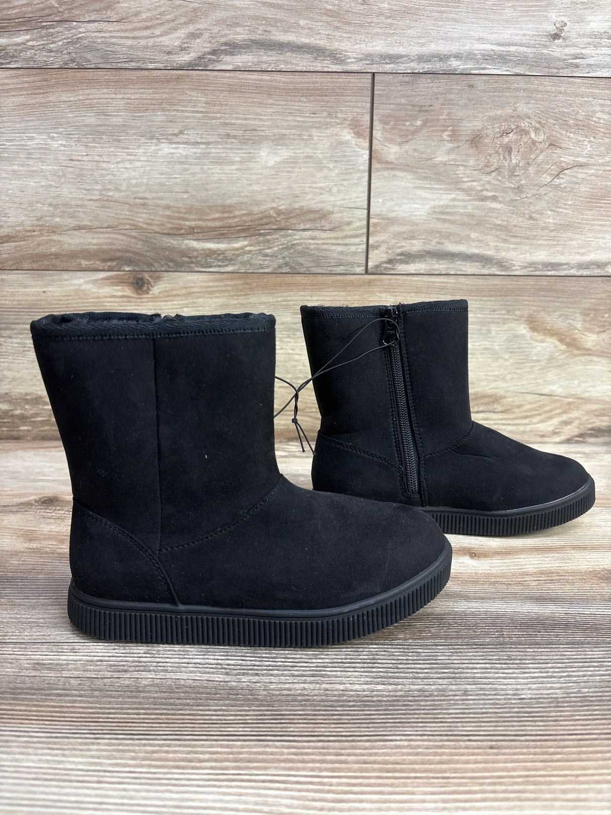 Pair of black children's winter boots with side zipper on wooden floor and background