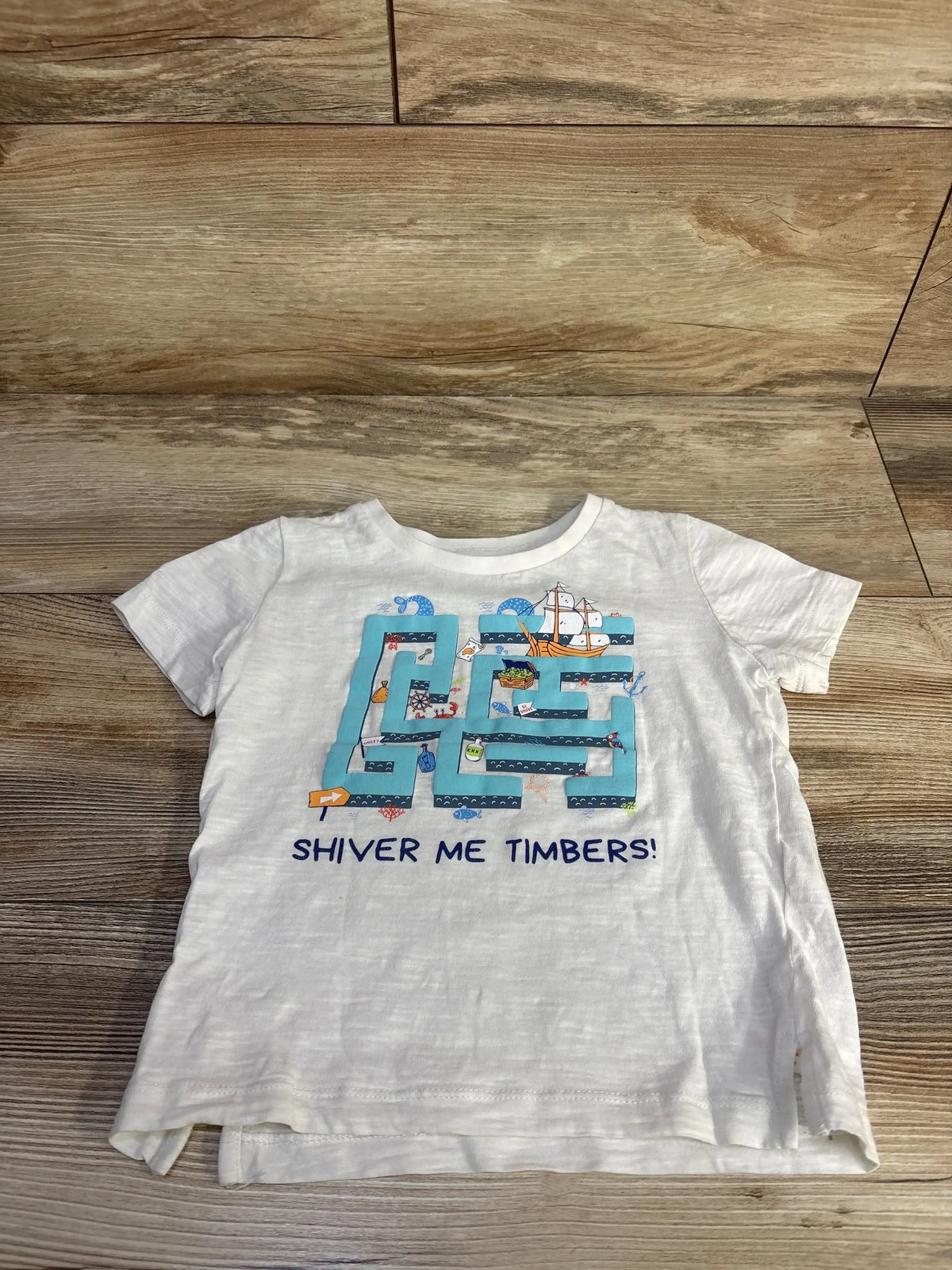 Flat lay white Cherubino toddler shirt (3T) with blue maze and ship graphic and SHIVER ME TIMBERS text on wood background
