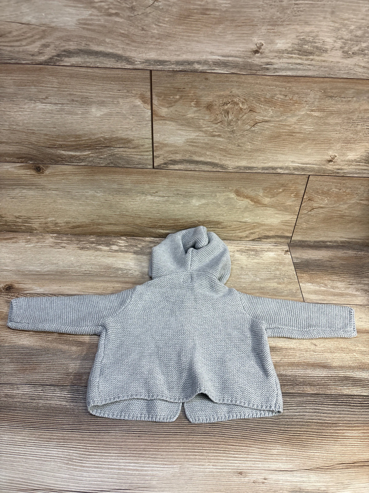 Front view of Baby Gap grey knit hooded cardigan in size 6 to 12 months showcasing hood and long sleeves on a wood floor