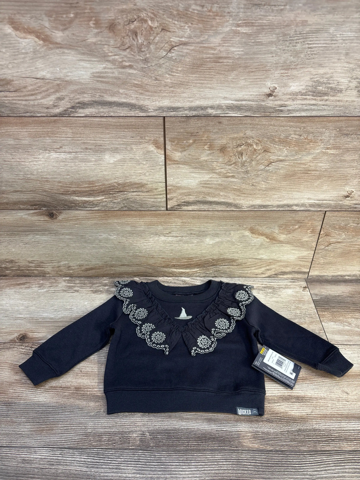 Front view of grey Modern Moments x Wicked Elphaba eyelet ruffle sweatshirt showcasing layered scalloped eyelet trim with a wood background