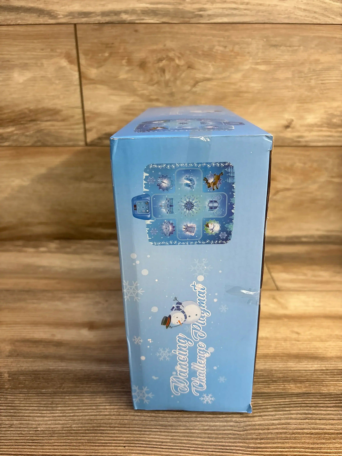 Side view of Frozen themed electronic dance mat box showing snowman artwork and playmat icon with wooden floor background