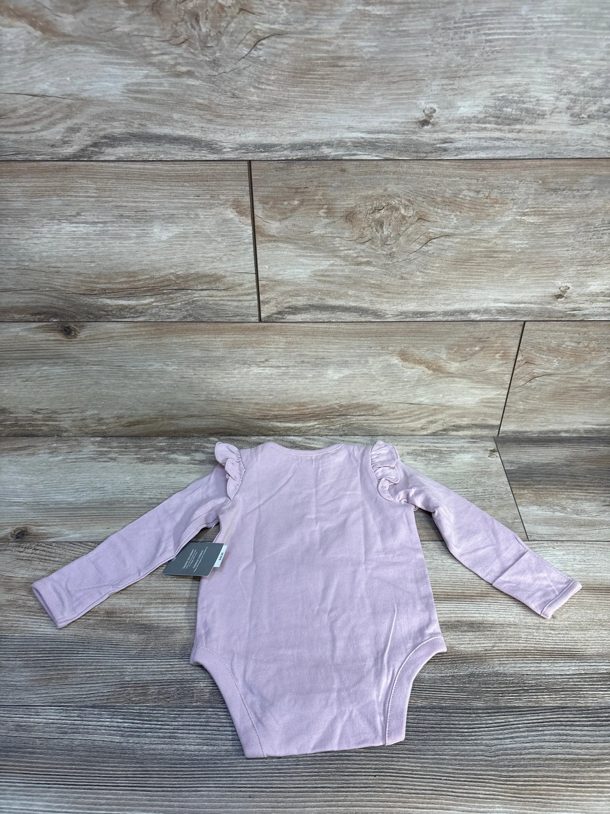 Front view of pink Baby Gap long sleeve bodysuit showcasing ruffled shoulders on a wood floor