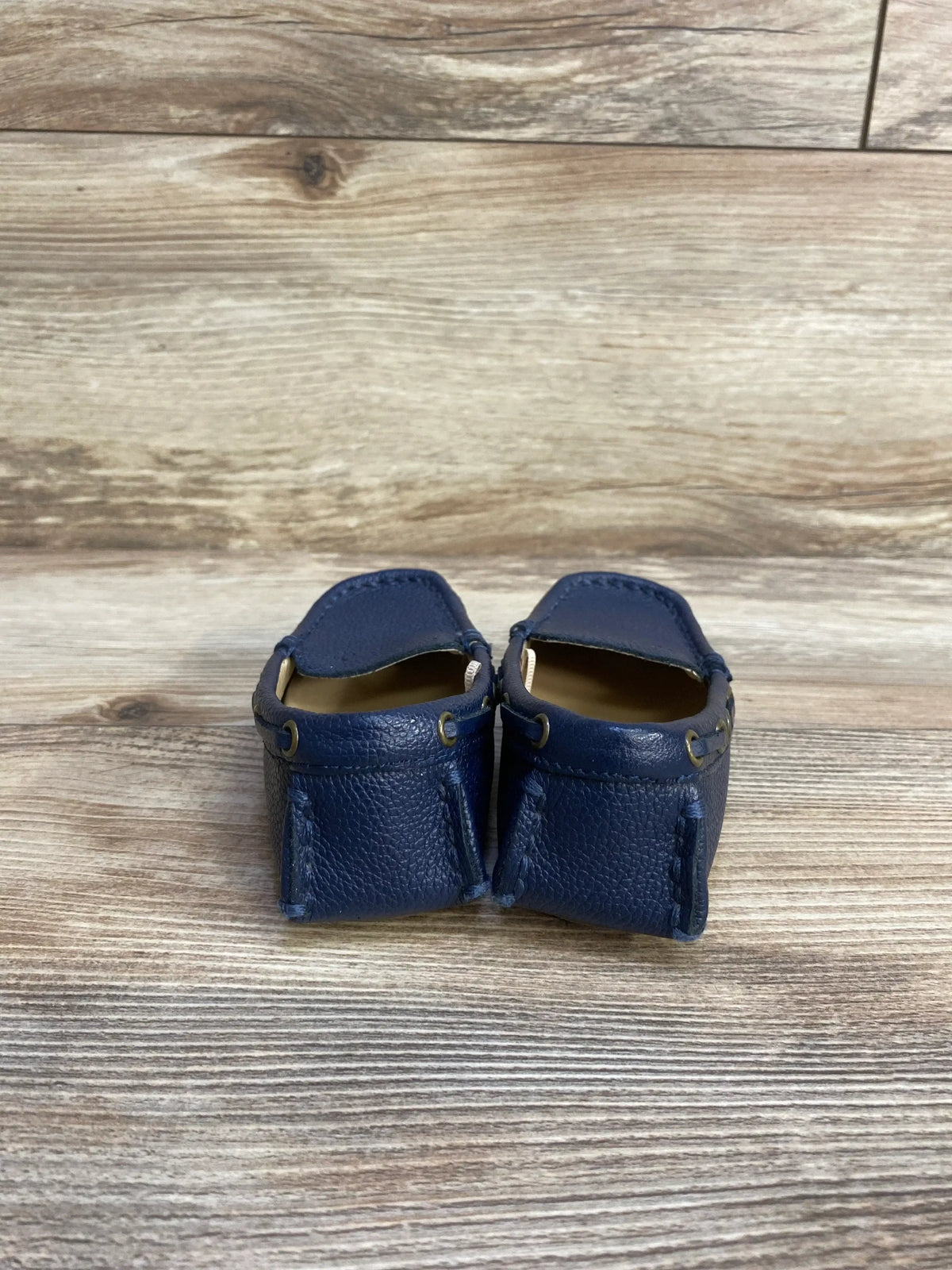 Back view of Janie and Jack navy leather driving shoes sz 8c showcasing pebbled leather upper and tan interior on wood plank floor