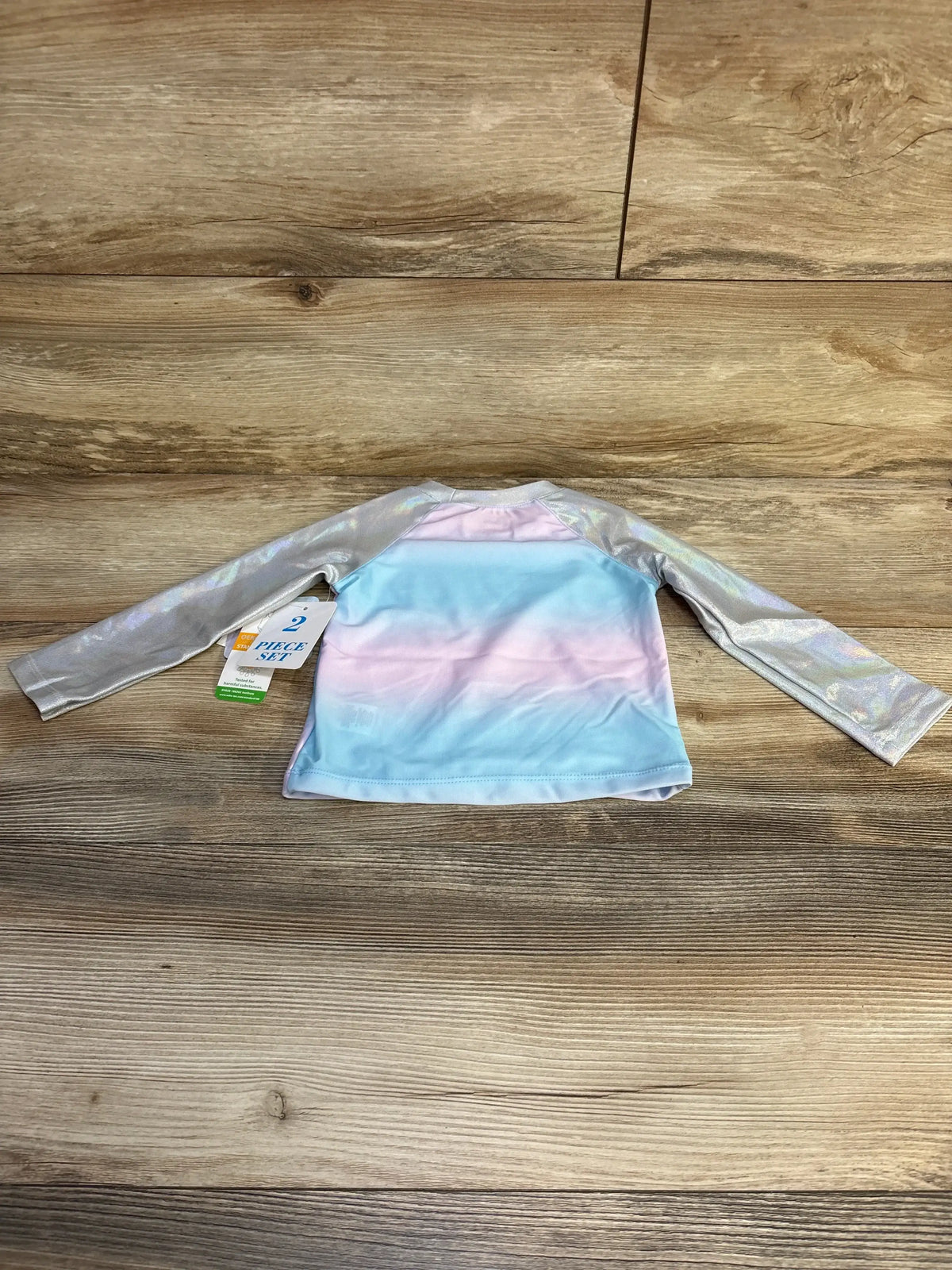 Back view of toddler Disney Frozen Elsa rashguard showing pastel blue-pink gradient body and iridescent silver sleeves on wood background