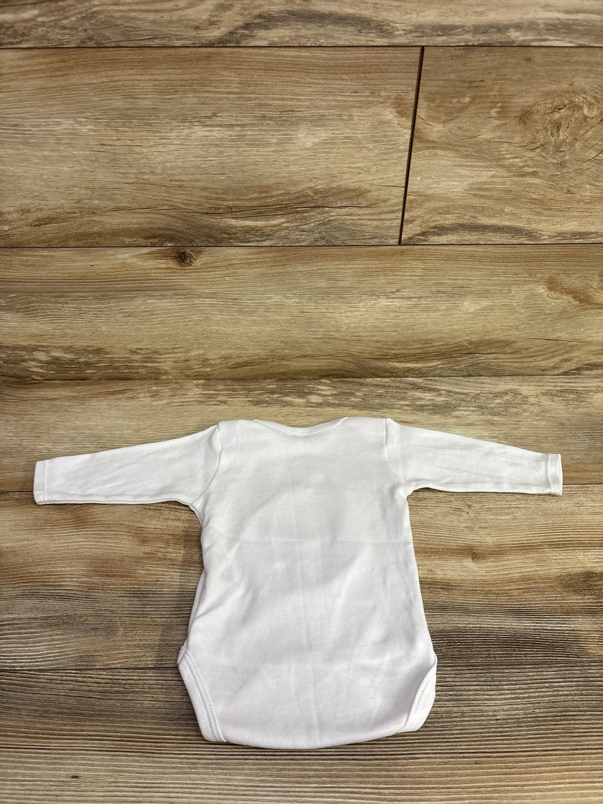 White long-sleeve baby bodysuit on wooden floor background