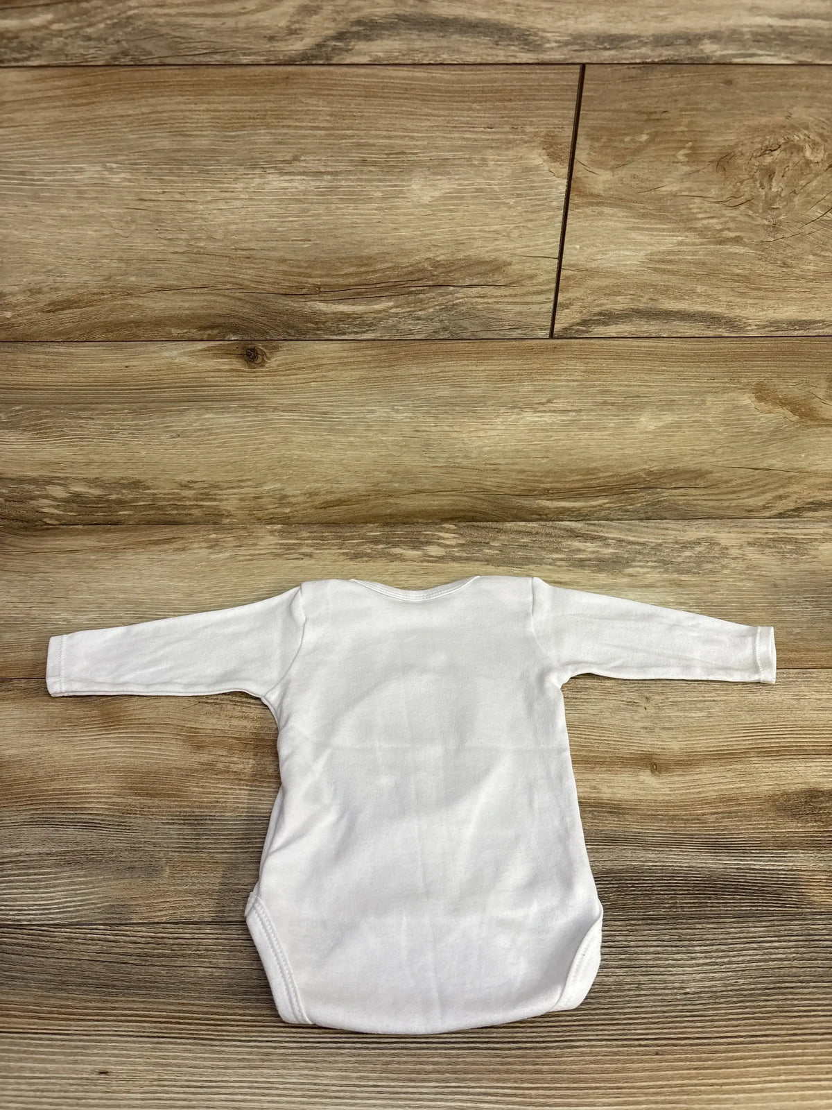 White long-sleeve baby bodysuit on wooden floor background