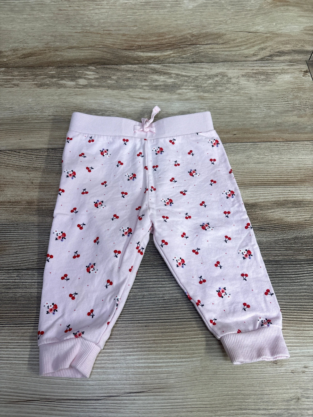 Light pink toddler pants with red cherry and flower print, ribbed cuffs and waistband on wooden floor