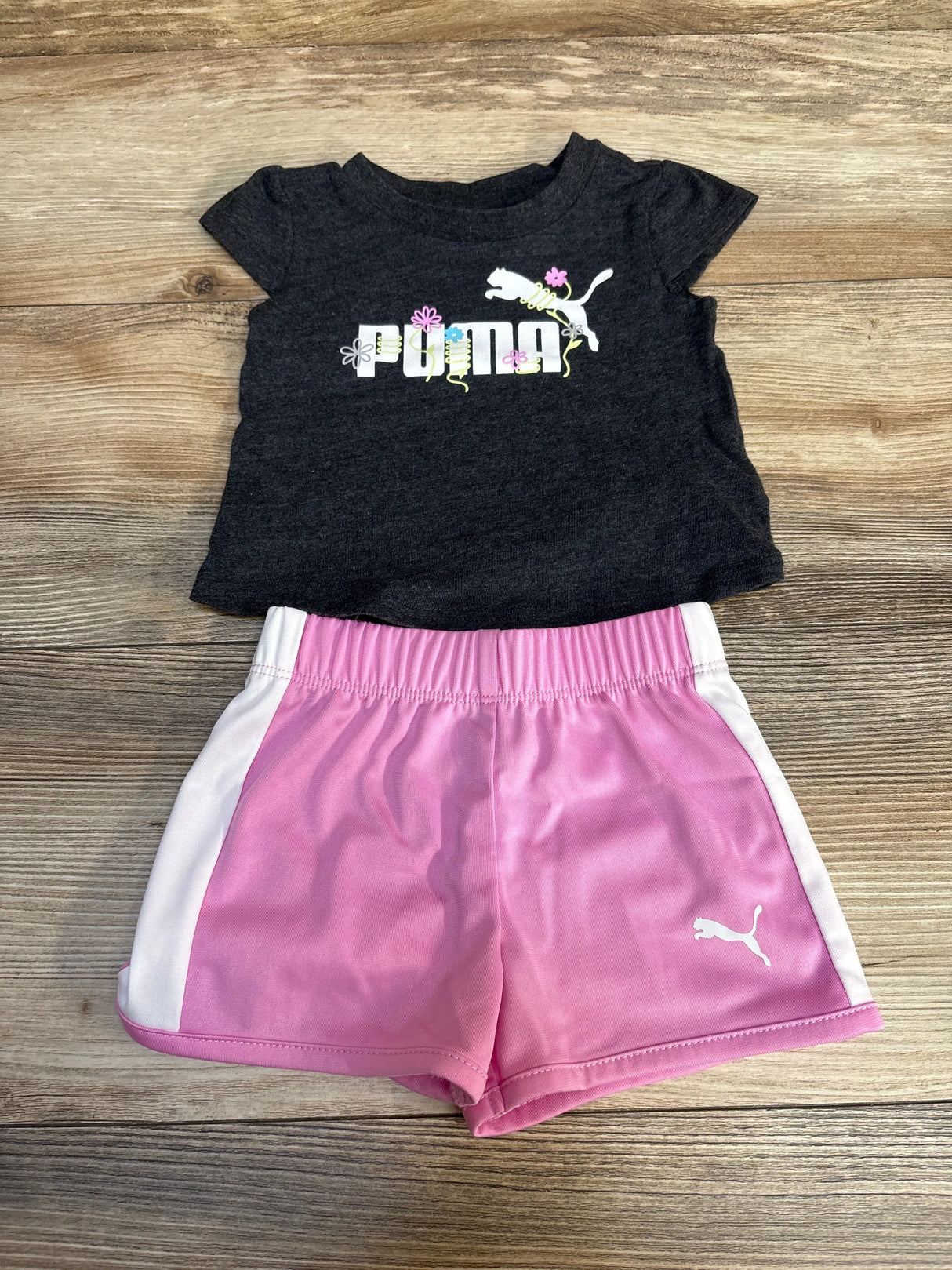 Girls' Puma black t-shirt with floral logo and pink athletic shorts set, flat lay