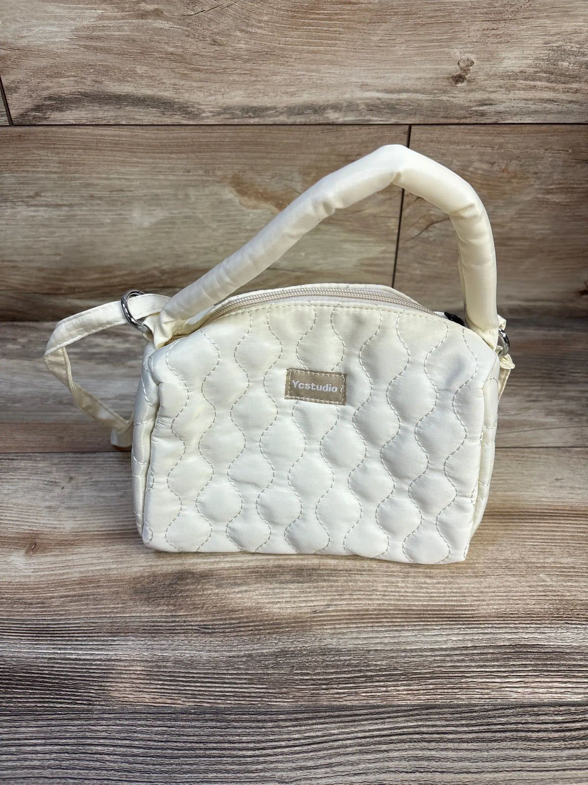 Front view of Ycstudio mini crossbody quilted bag showcasing ivory padded texture, top handle, and crossbody strap on wood