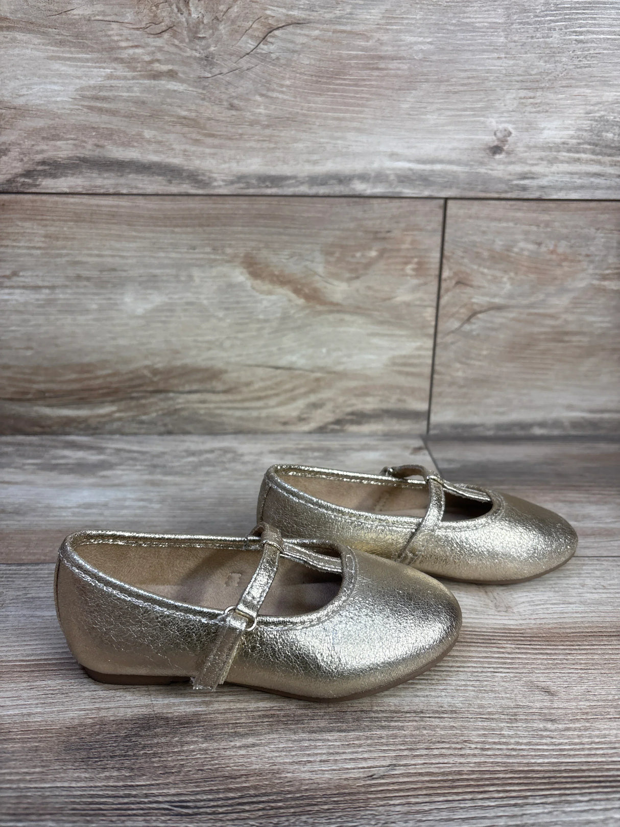 Side view of Jumping Beans Susie T-strap ballet flats in metallic gold size 8C showing T-strap and rounded toe on wood floor