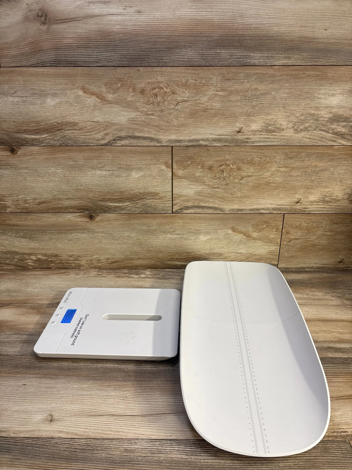 Angled view of MomMed Baby Scale showcasing white infant tray with height markings and blue digital display on a wood surface
