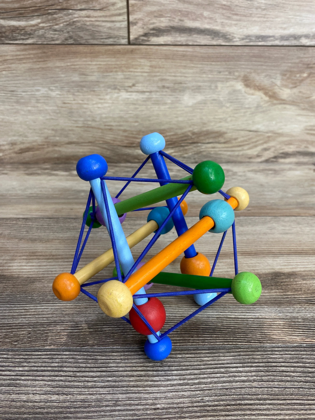 Colorful wooden baby toy with balls and rods connected by blue elastic strings on wooden surface