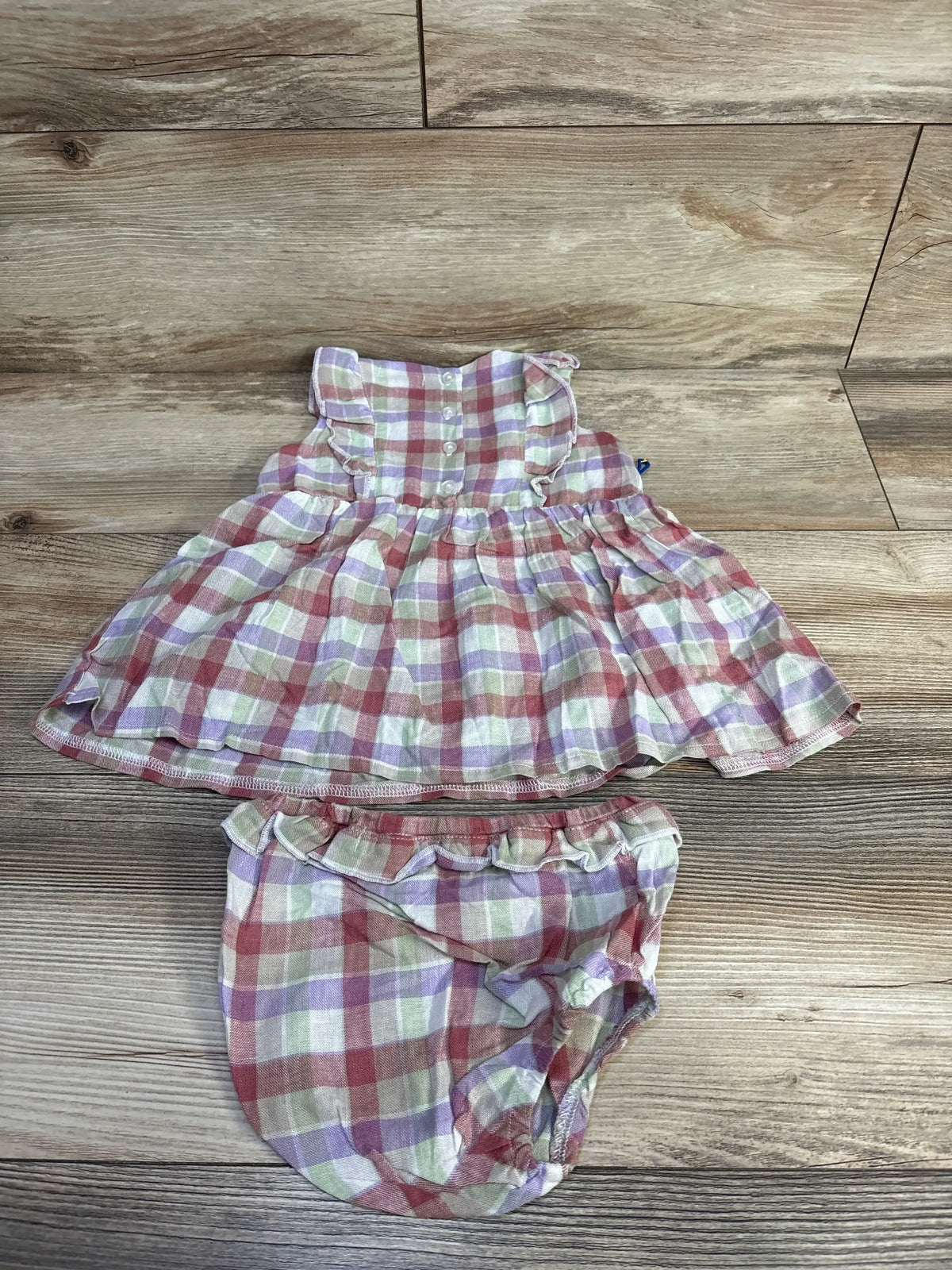 Front view of Maison Me Baby pastel plaid ruffle dress and bloomers set with sleeveless ruffled dress on wood background