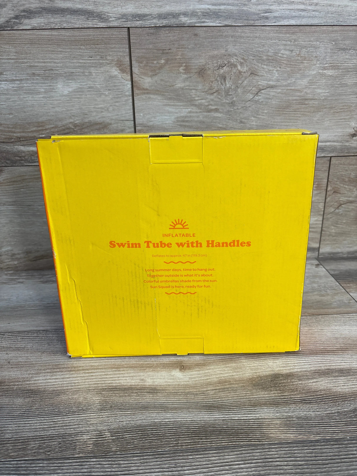 Yellow box labeled inflatable swim tube with handles on wood floor, kids pool float packaging
