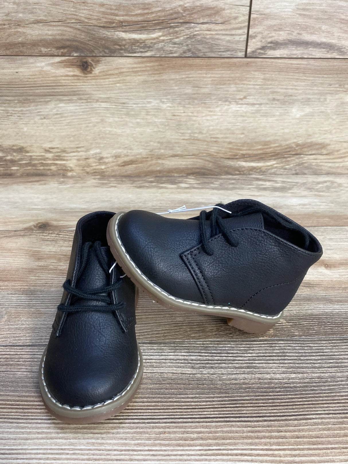 Black toddler lace-up boots with tan soles on wood floor background