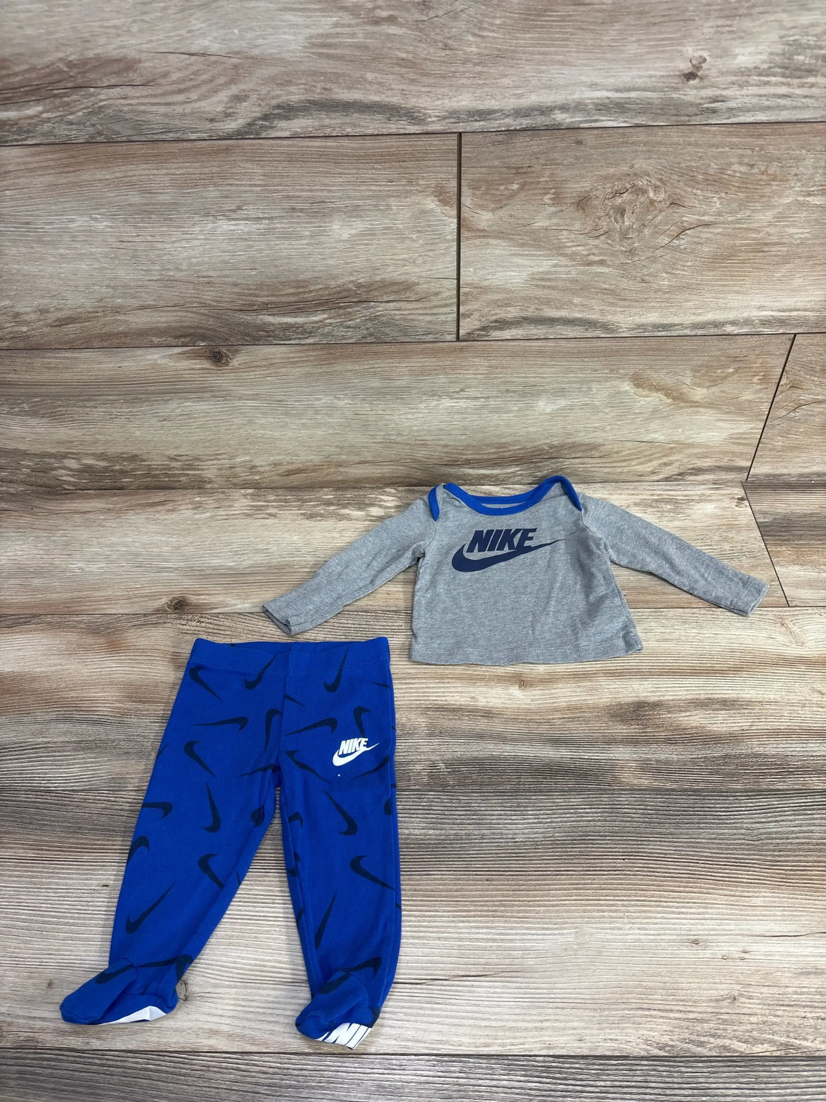 Nike baby outfit with grey long-sleeve top and blue pants with black logos on wooden floor