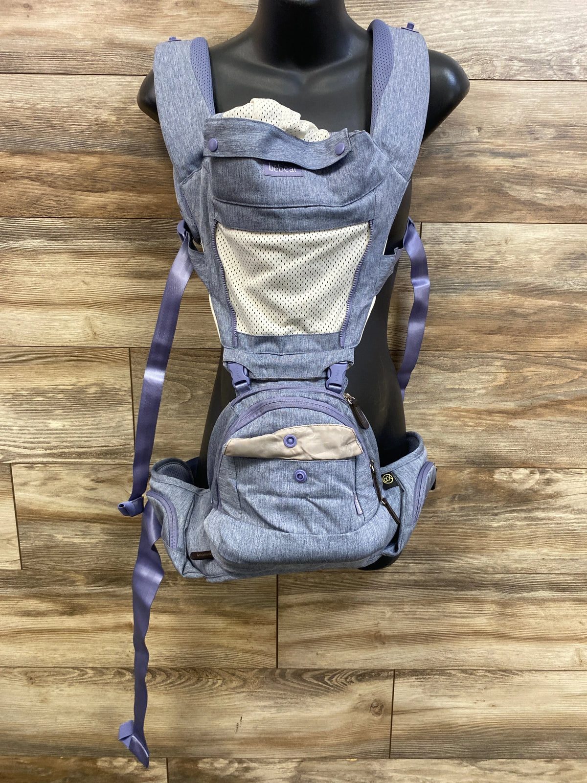 Front view of Bebear 2-in-1 Bebamour detachable hip-seat baby carrier in blue showing mesh infant panel, zippered hip-seat pocket and padded shoulder straps on wood background