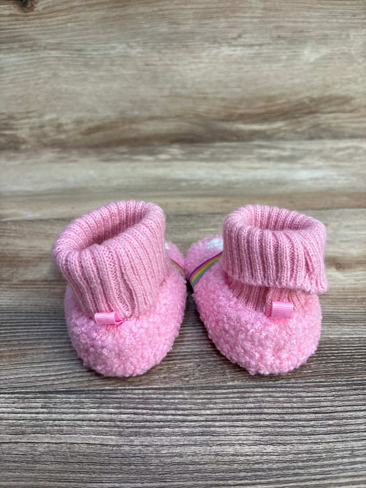 Pink knit baby booties with ribbed cuffs on a wooden surface