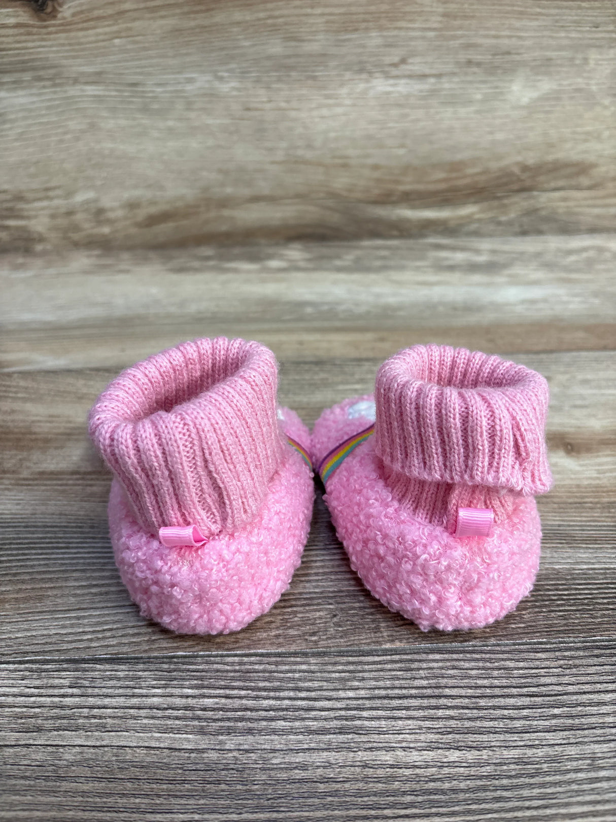 Pink knit baby booties with ribbed cuffs on a wooden surface
