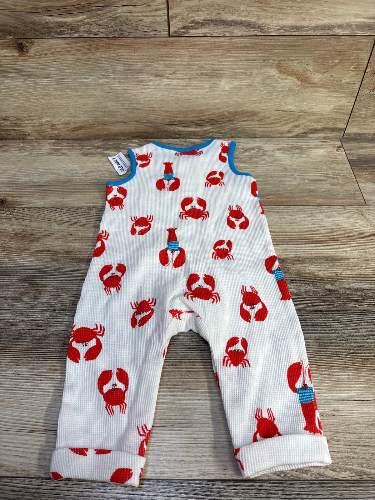 Top view of baby sleeveless waffle-knit Henley jumpsuit by Old Navy with red crab print, blue trim and rolled cuffs on wood