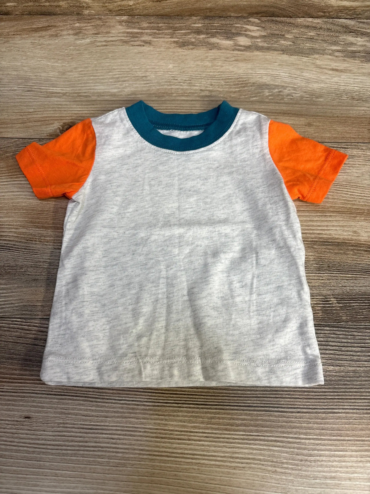 Front flat lay of short sleeve baby shirt with light gray body, orange sleeves and teal collar on wood background