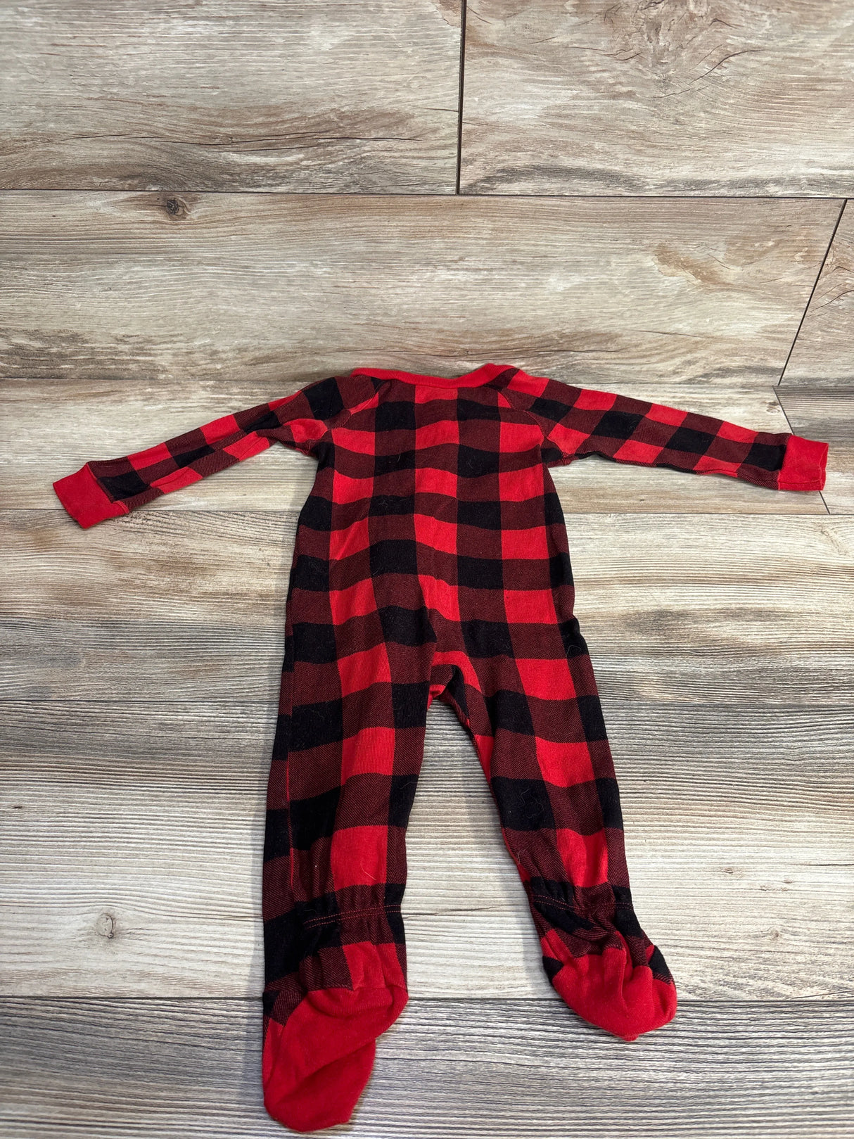 Red and black plaid footed baby sleeper on wood background, long sleeves, cozy kids clothing