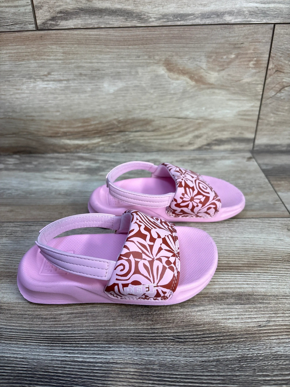 Front view of Reef pink floral sandals showcasing patterned straps and heel straps on a wood-look background