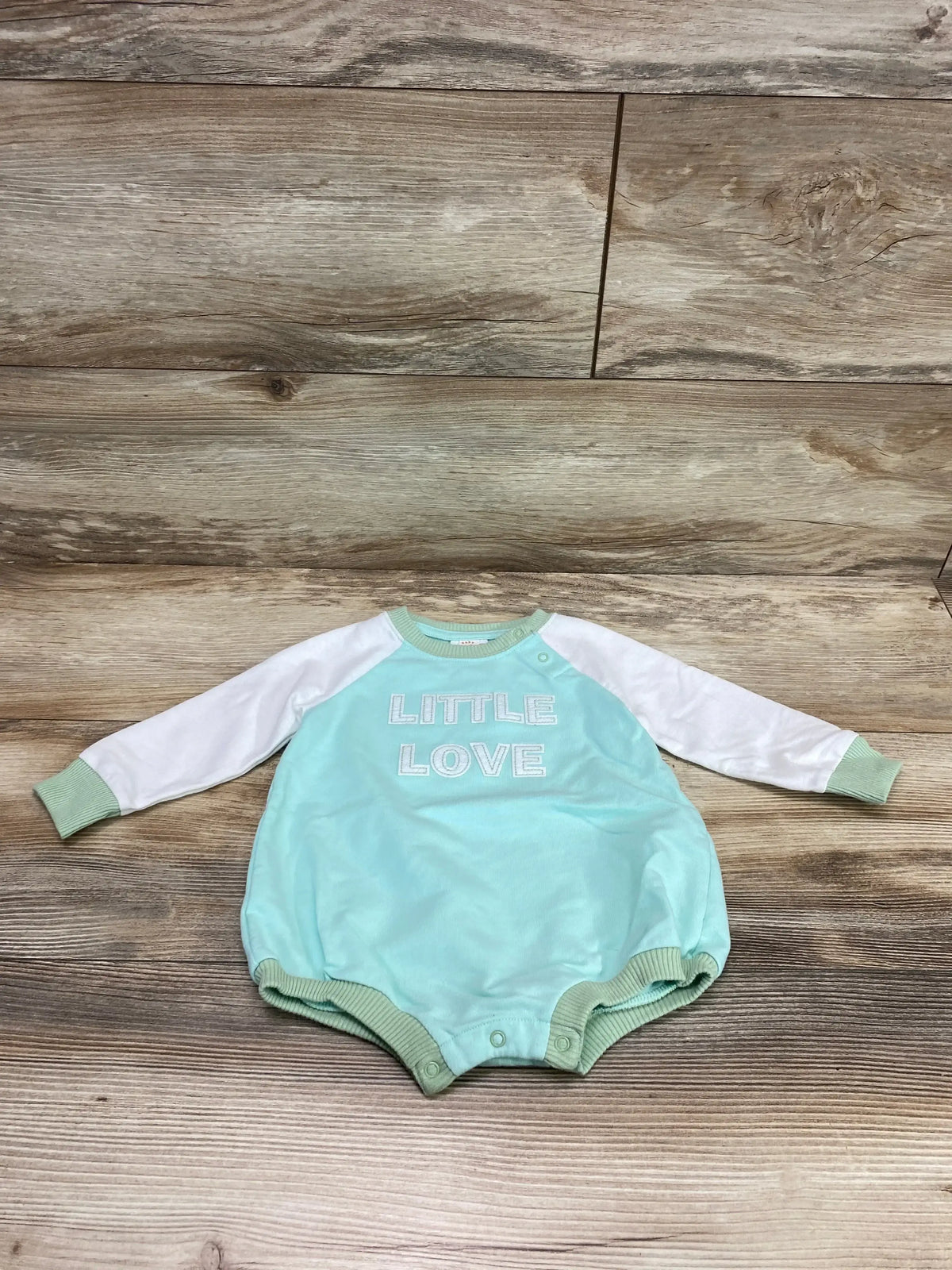 Flat lay of Cat and Jack baby romper, mint body with white sleeves, LITTLE LOVE chest text, snap crotch on wood floor