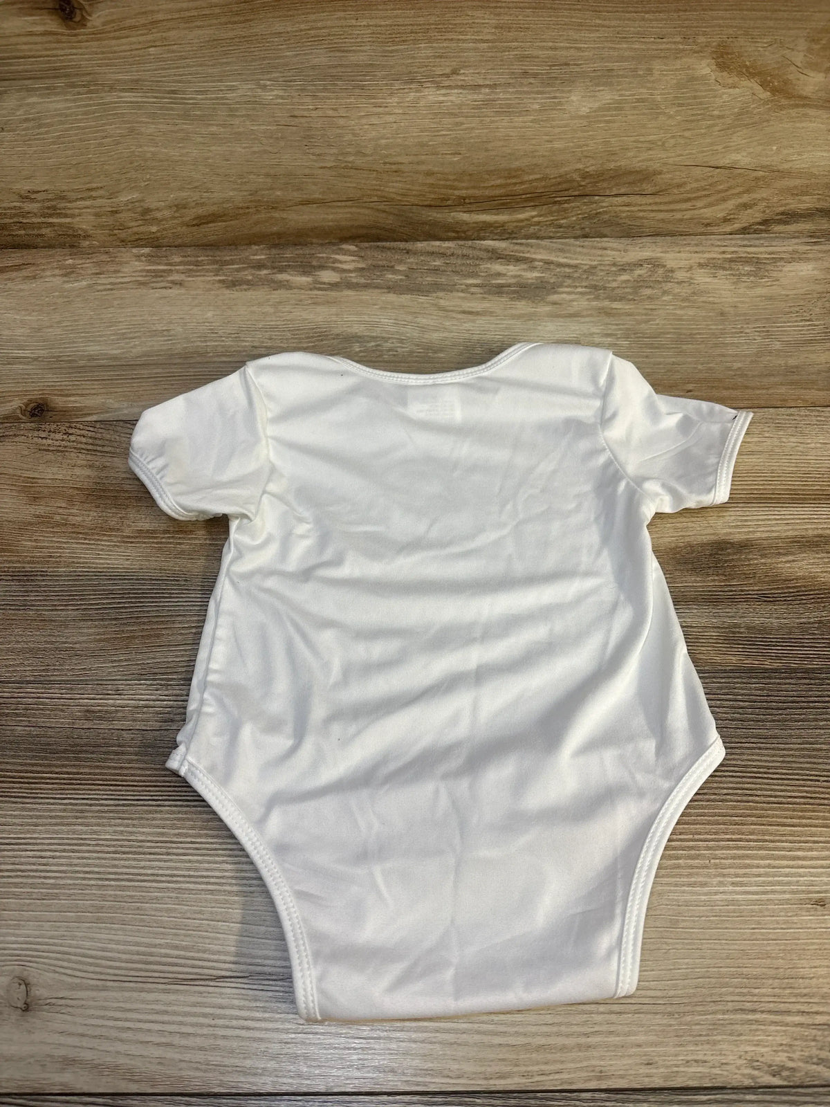 White short sleeve baby bodysuit on wooden background, gently used infant clothing