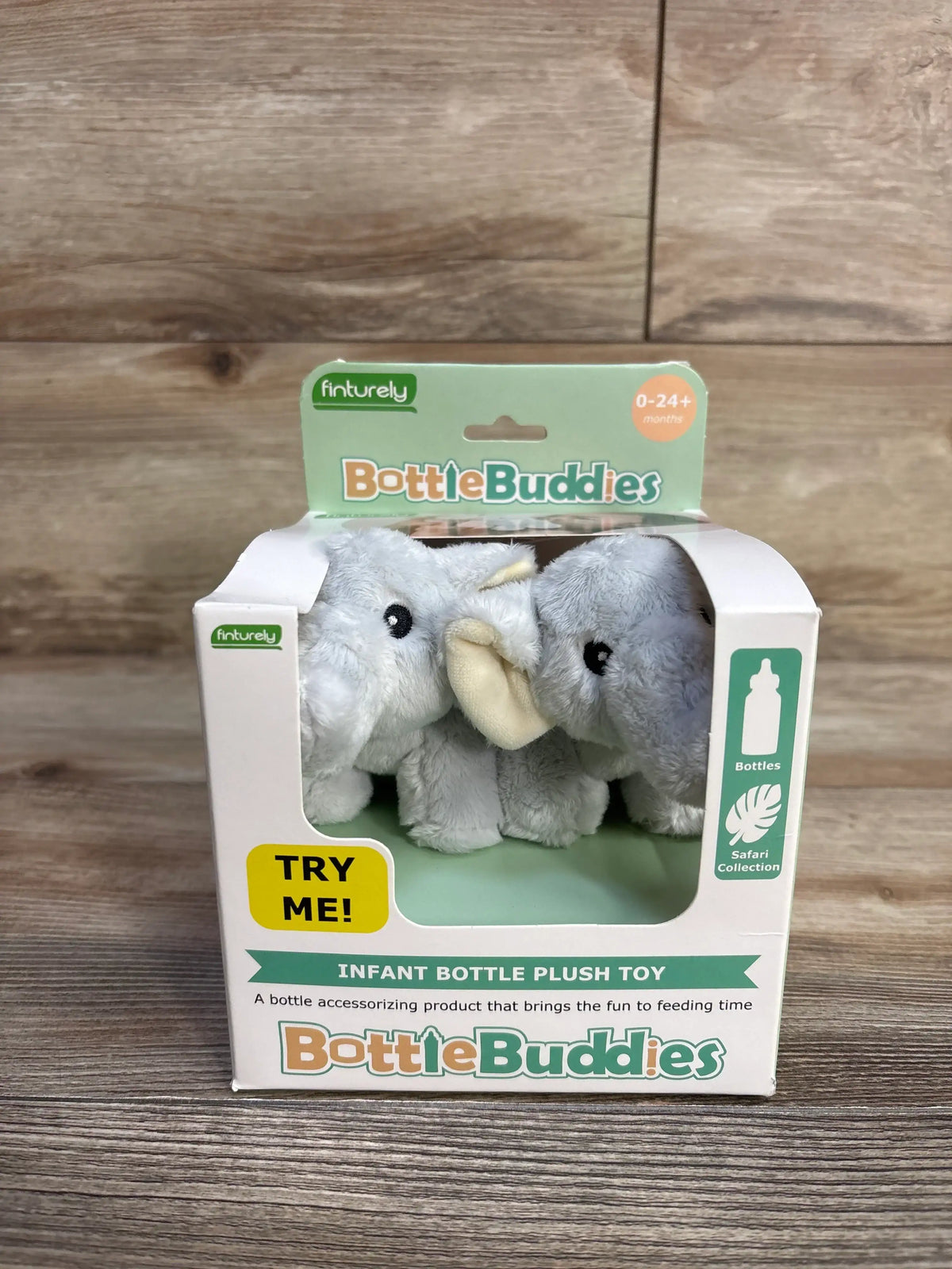 Front view of BottleBuddies elephant plush starter kit showing two grey elephant bottle toppers in window box with yellow TRY ME sticker on wooden surface