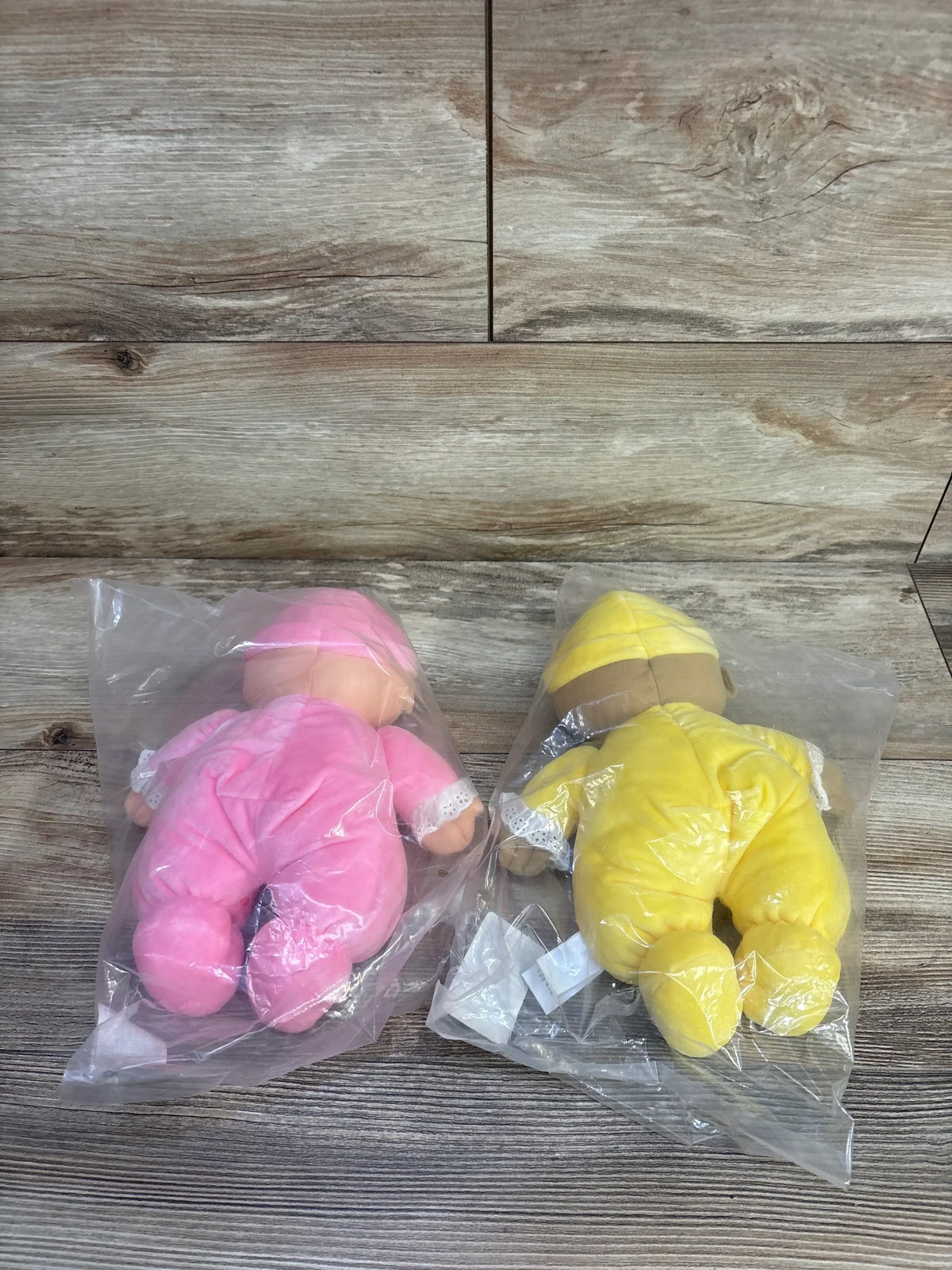 Back view of two Lakeshore Cuddly washable dolls from the four-piece set, in pink and yellow clothing on a wood-grain floor