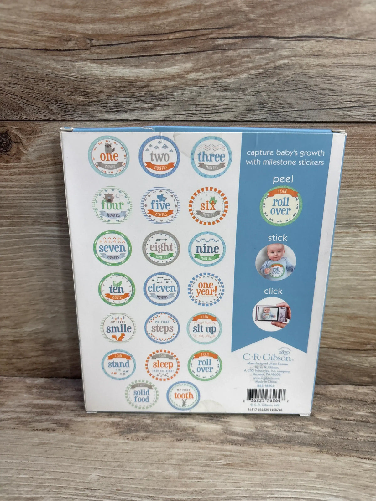 Back of Baby's First Year belly stickers box showing round monthly and milestone stickers on wood surface