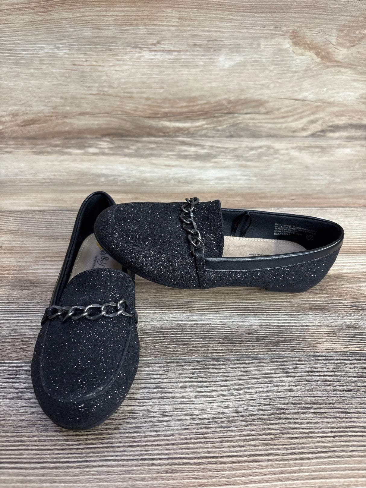 Pair of black glitter loafers with metal chain detail on wood surface
